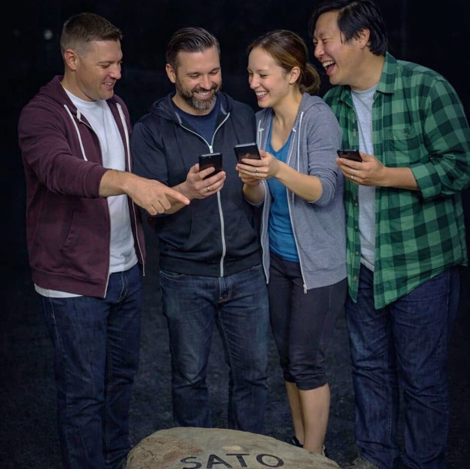 Squadra di giocatori collabora risolvendo un enigma con smartphone nell’escape game outdoor Sato Code
